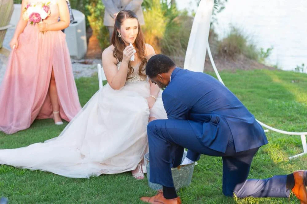 Interracial bride and groom performing a foot washing ceremony